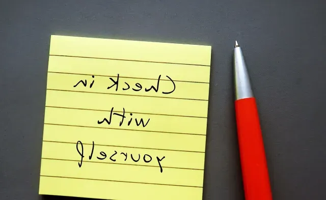 Note paper on gray background with handwritten text - Check in with yourself - carving out time each day to ask yourself how you're doing