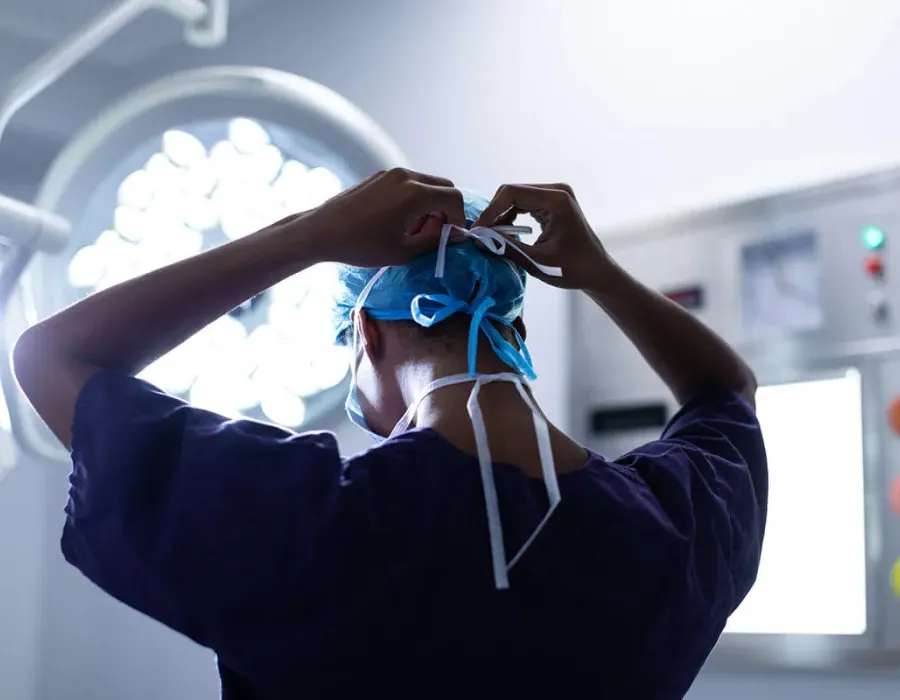 Surgical technologist fastening mask in preparation before surgery in operating room